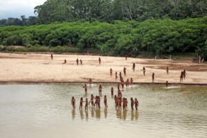people in loincloths walking from a sandy riverbank into water