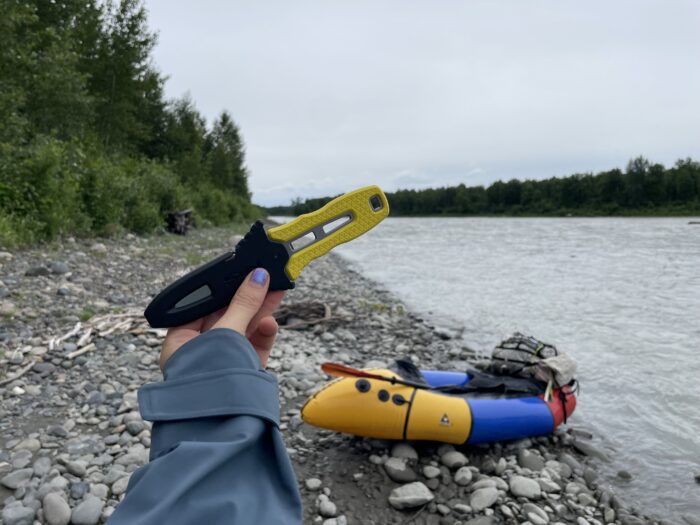 Chelsey holds the NRS Pilot Knife in front of her packraft. 