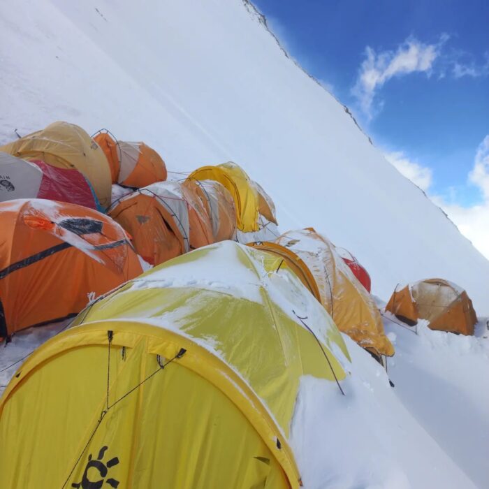 Tents lines up on a steep slope and semi covered in snow. 