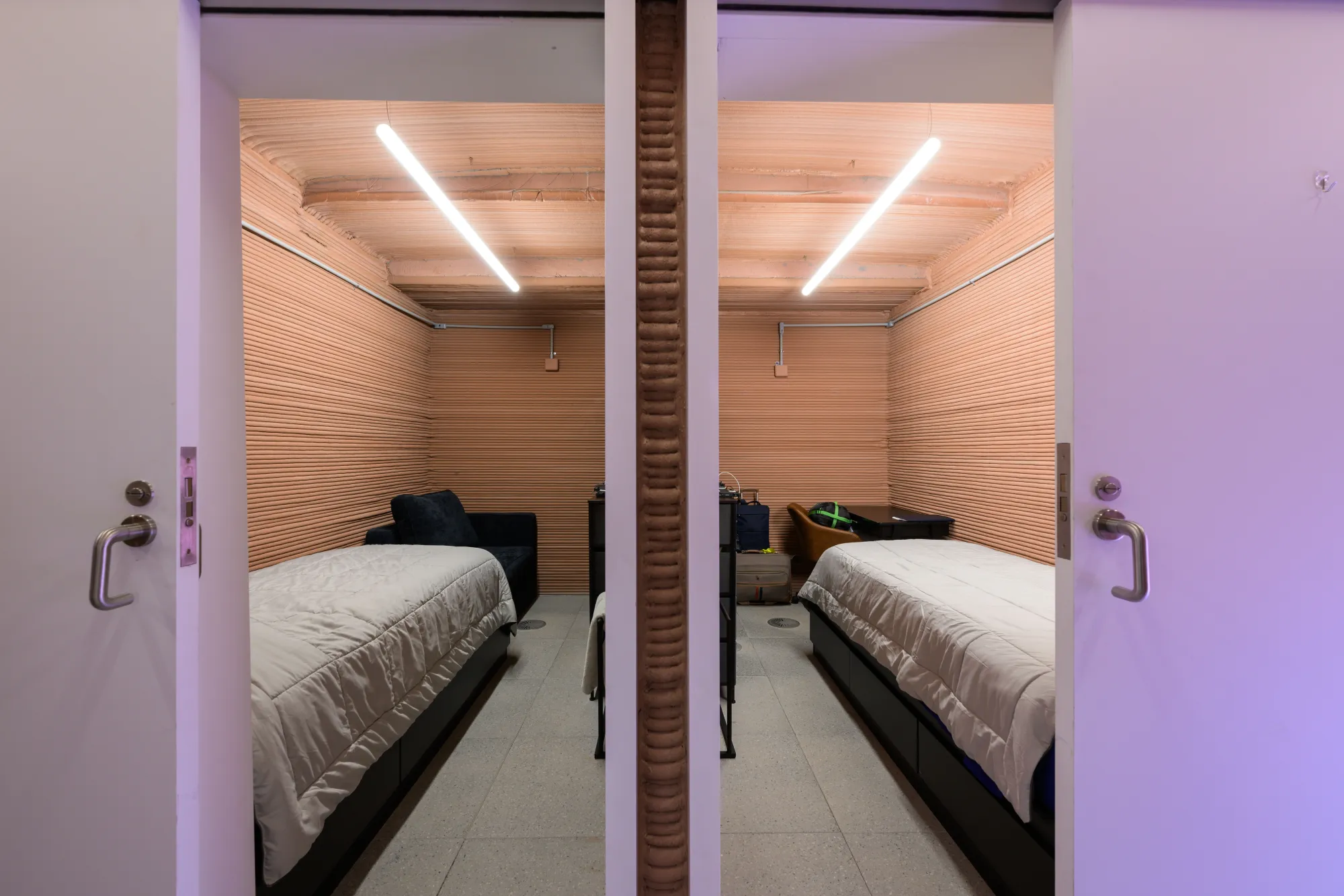 Photograph through the doorway looking in on two private quarters separated by a wall. Each room has polished wood walls and a twin bed occupying most of the space.