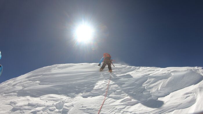 A climber about to reach the top of a snow cornice.