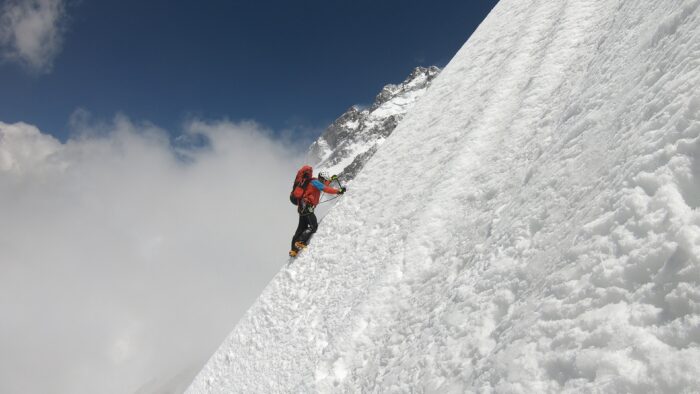 A climber traversing a steep snow slope on Muchu Chhish