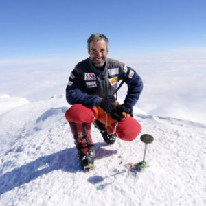 The climber and pilot squatting on a summit, possibly Vinson