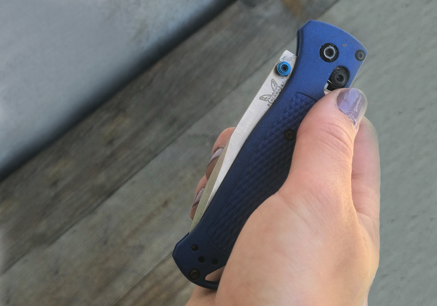 Kirby holds a folded, blue Benchmade Bugout knife. 