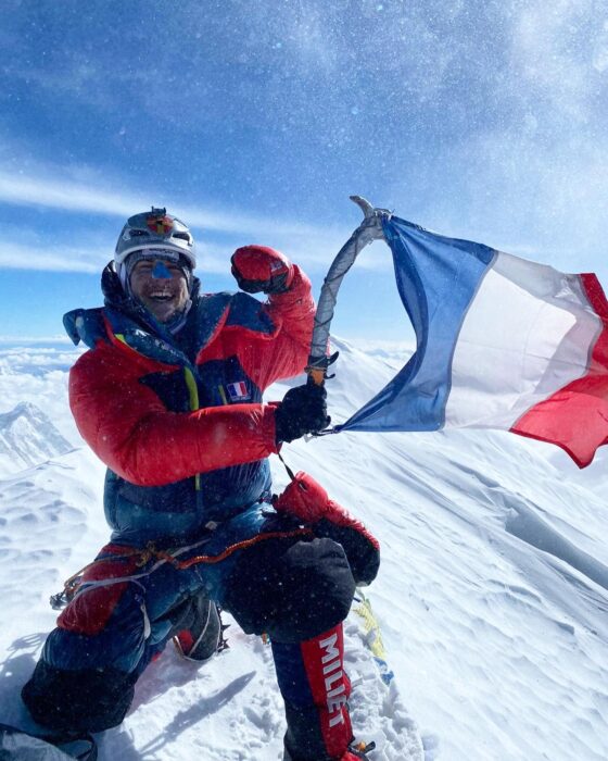 the climber on a windy , snowy summit, holding a French flag attached to his ice-axe