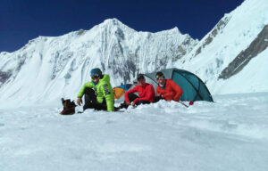climbers in front of a tent on a flat plateau surrounded by peaks