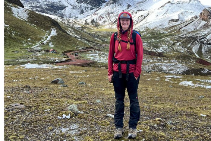 Chelsey is wearing black hiking pants and a red sun shirt while hiking in Peru.