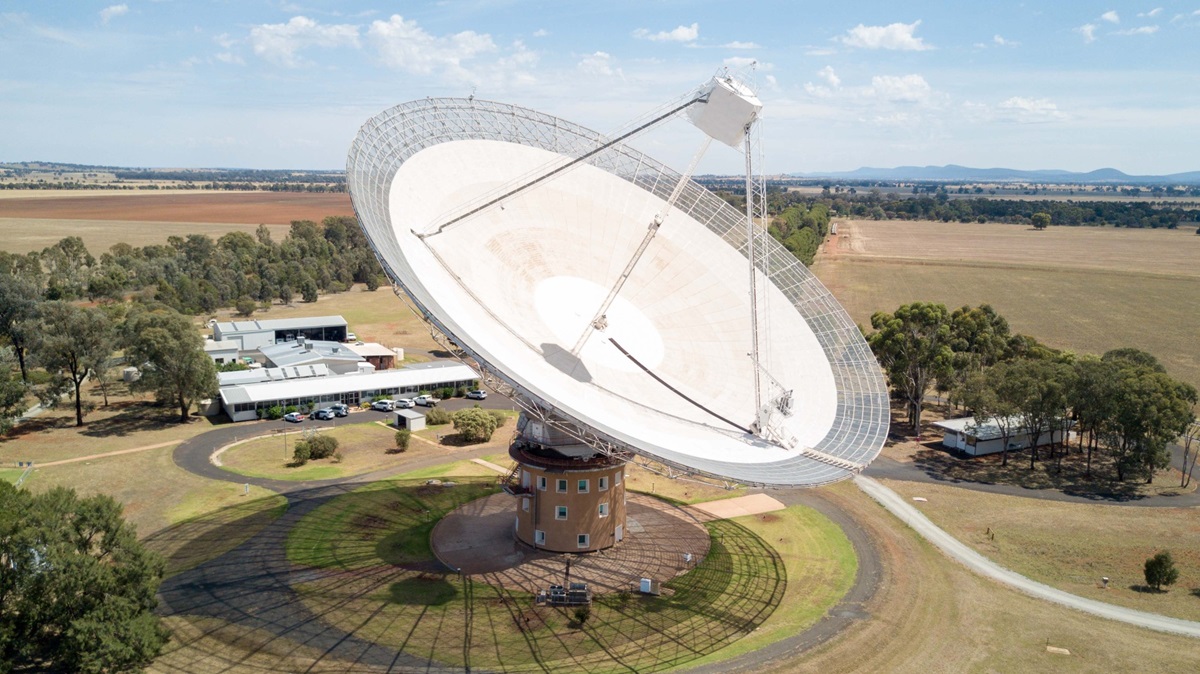 A large radio telescope sits in a flat field.