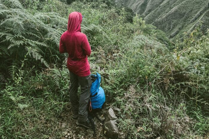 Chelsey stands with her back to the camera, wearing a baggy red sun shirt. The backdop is dense and jungle-looking, in Peru.