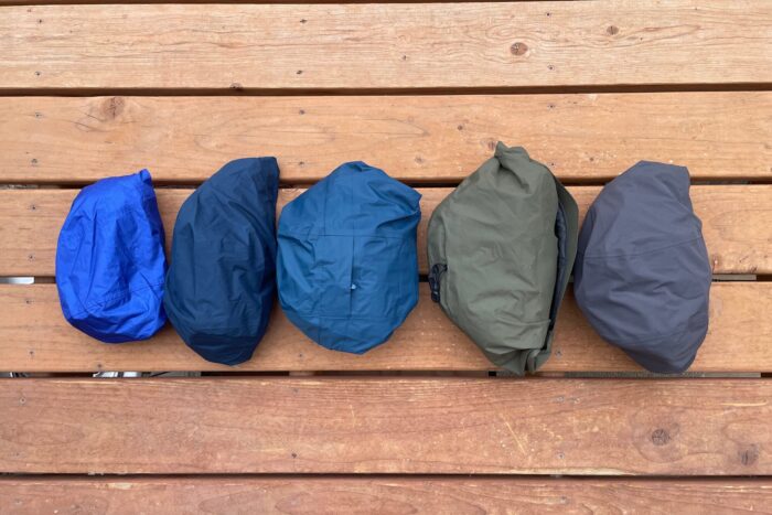 Five rain jackets are shown packed into their own hoods to demostrate packed size. 