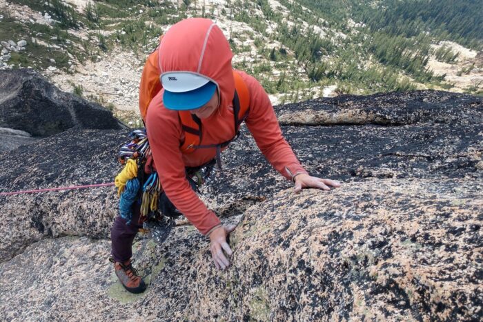 Chelsey is leading a rock climb in the PNW. She's wearing hiking pants and a red sun hoody.