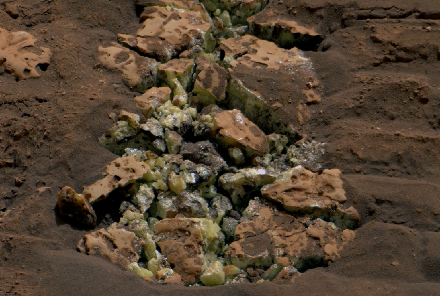 A photo of a Martian rock which has cracked open to reveal yellow-green crystals.