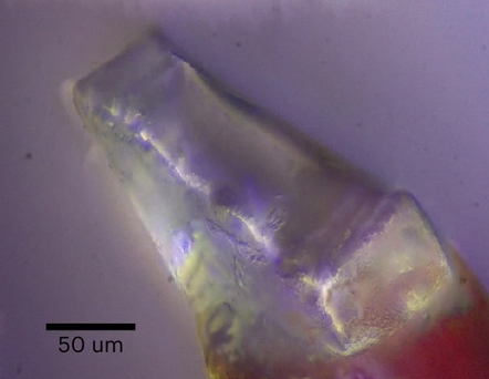 A microscopic photograph of a purple and green crystal. A scale label shows that the image is about 200 micrometers across.