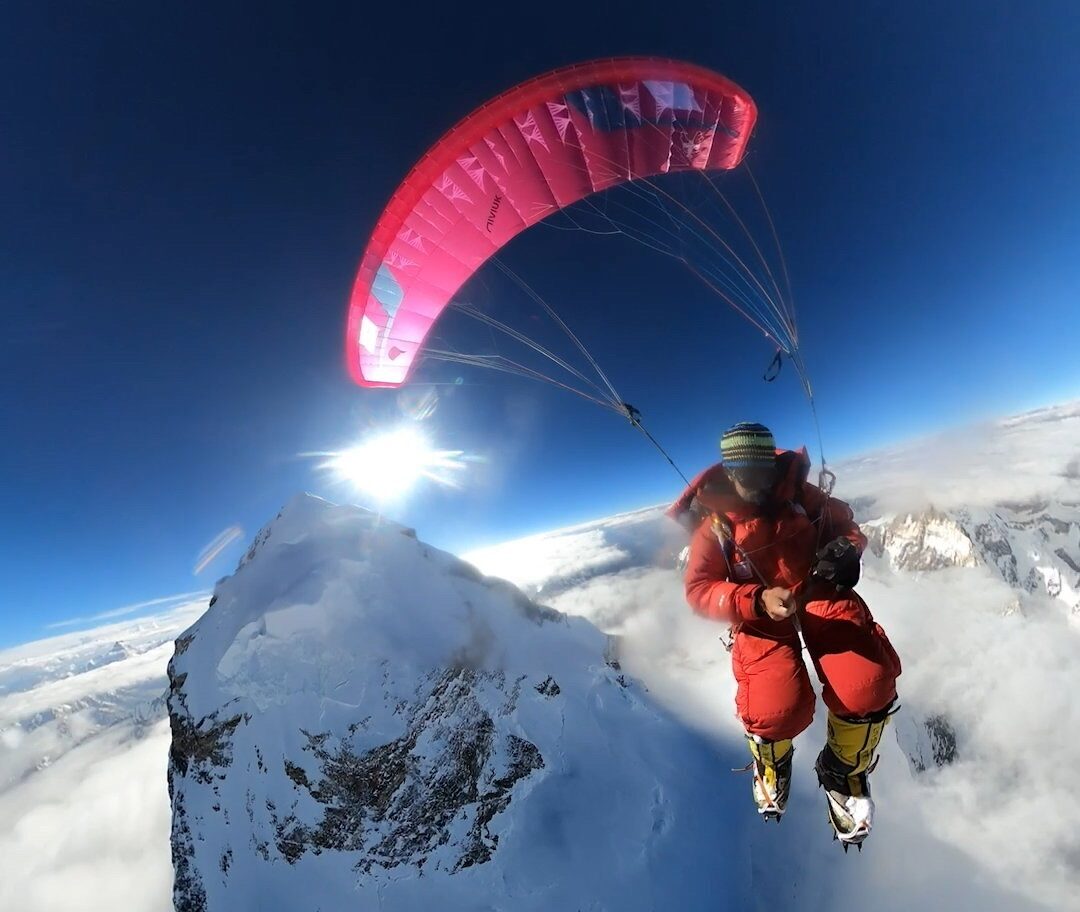 the paraglider takes a selfie with the summit of K2 behind him.