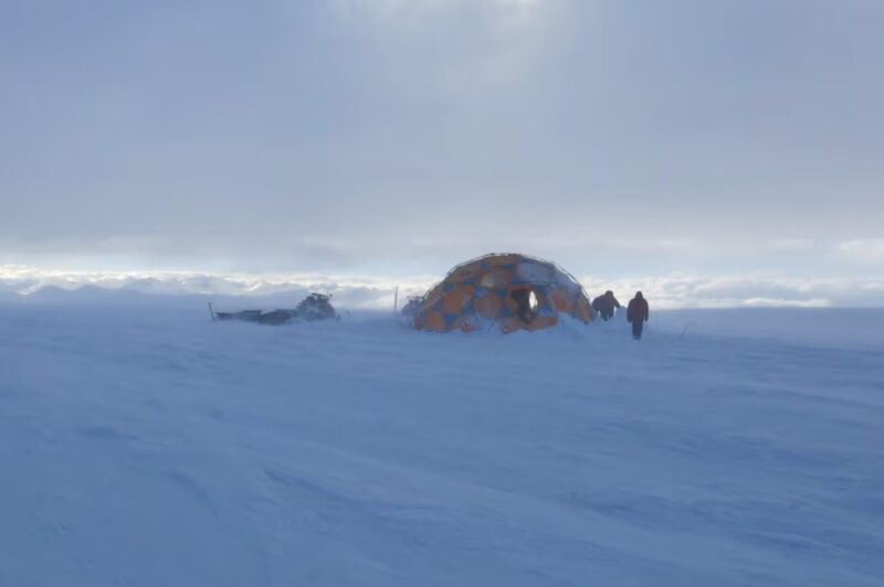 small figures beside tent on windy glacier