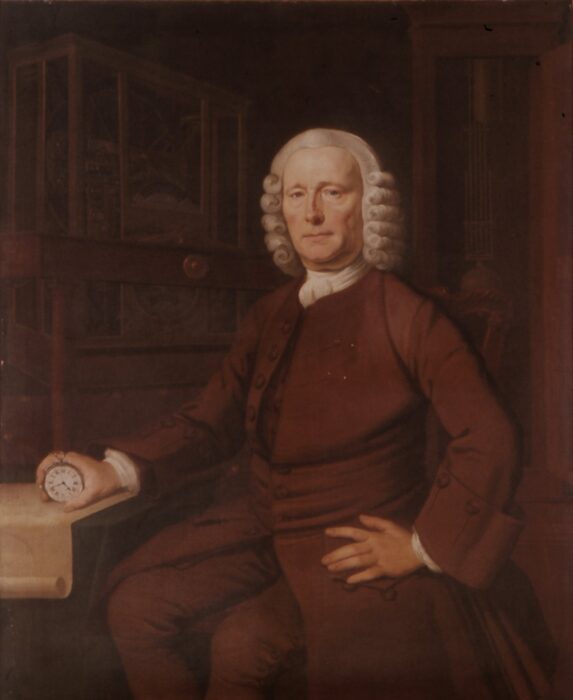 an elderly man in a wig holds a chronometer