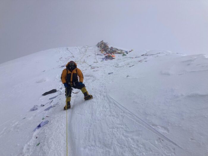 A Sherpa climber on Everest with the summit behind him in cloudy weather