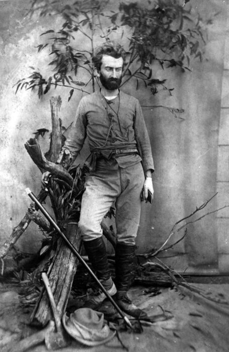 a photograph of a bearded man posing against a backdrop