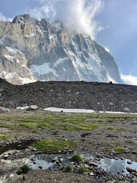 Grassy plains and a mixed rock and ice big wall in backgtround