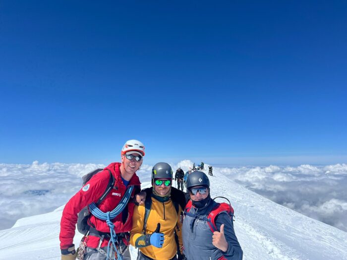 The climbers roped up on a wide summit with a sea of clouds in background