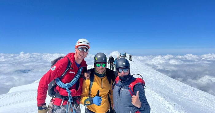 The climbers roped up on a wide summit with a sea of clouds in background