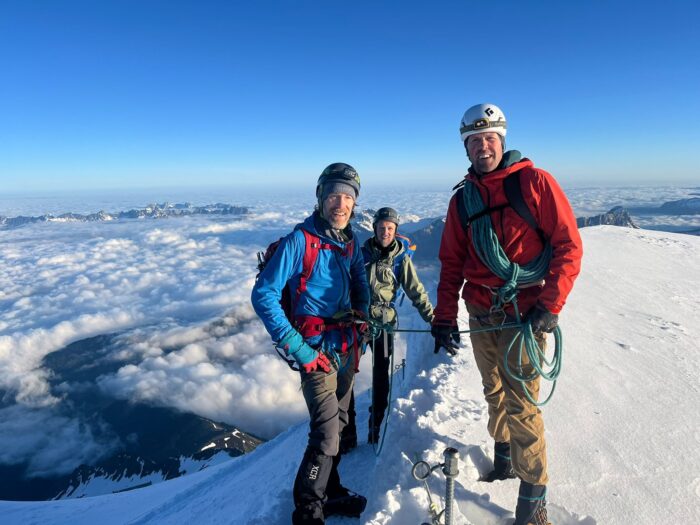 a guide with two clients on a snow ridge.