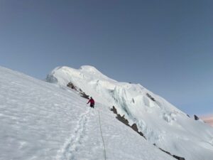 Climbers on a snow slope heading toward a corniced summit