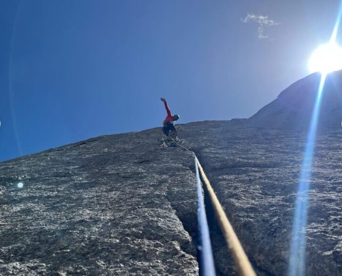 a climber waves his hand from a vertical granite wall, with a cack in the middle