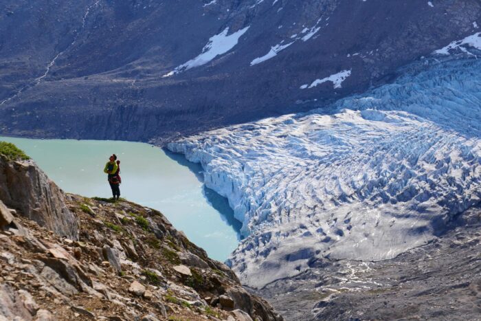 One of the team members at the base of the big wall, with a glacier reaching the sea shore in background