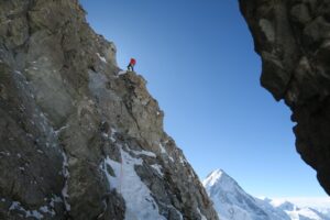 A climber on a ledge of a rocky ridge on Gasherbrum III