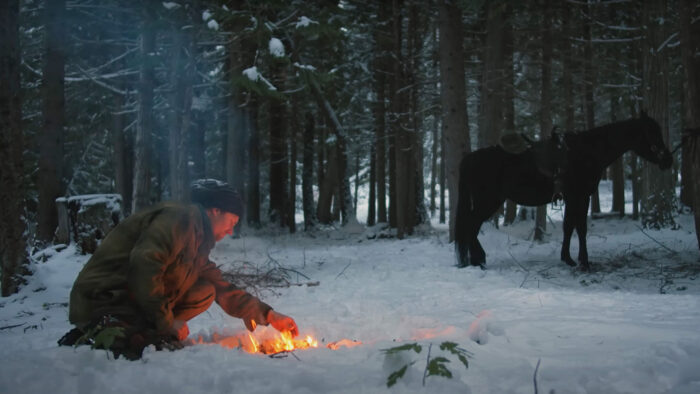 A man huddles around a campfire in the snow. 