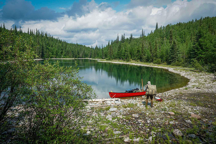 Canoeist packing up on shore of small wilderness lake