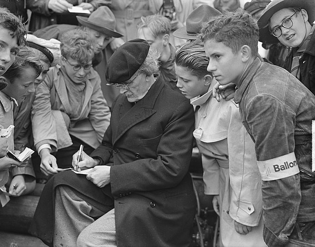 an old man surrounded by children signs autographs