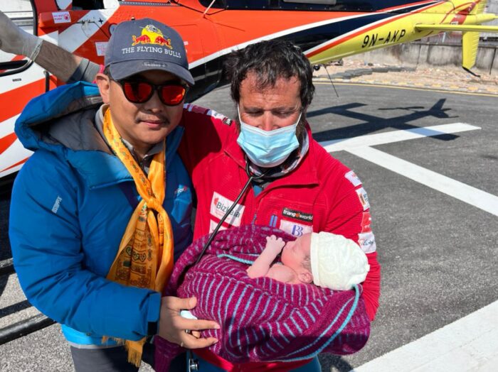 Txikon and helicopter pilot pose with a baby in front of a helicopter