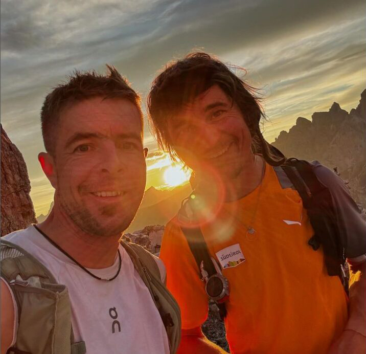 The climbers smile to the camera with the sun setting behind them