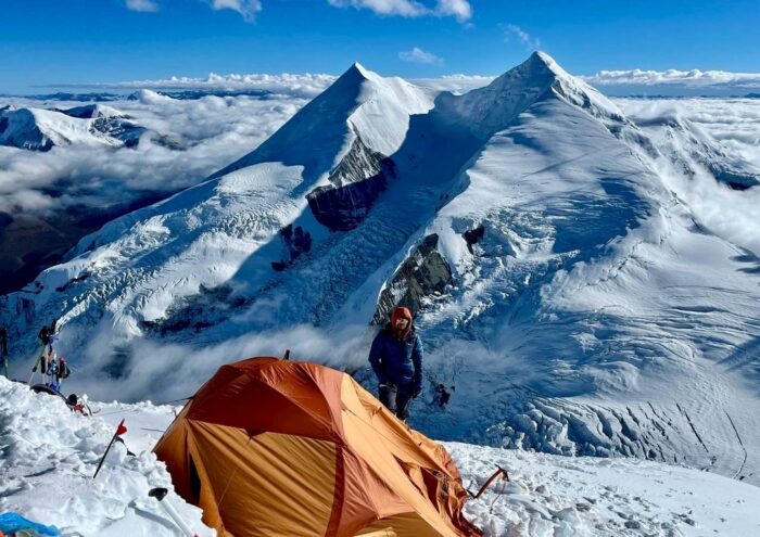 A climber by a lonely tent on snowy terrain on Dhaulagiri, some peaks behind