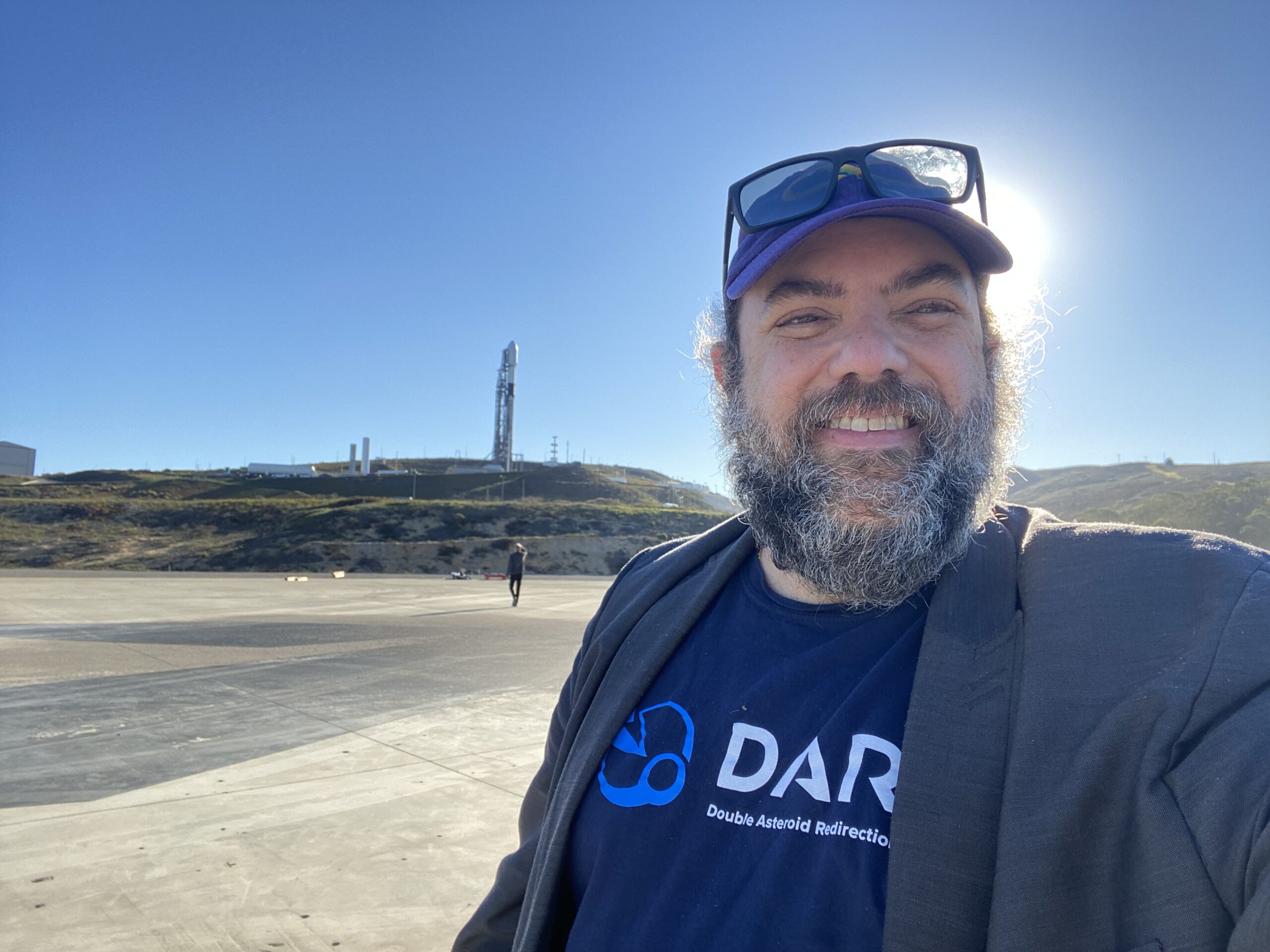 A man takes a selfie in front of a rocket launch pad.