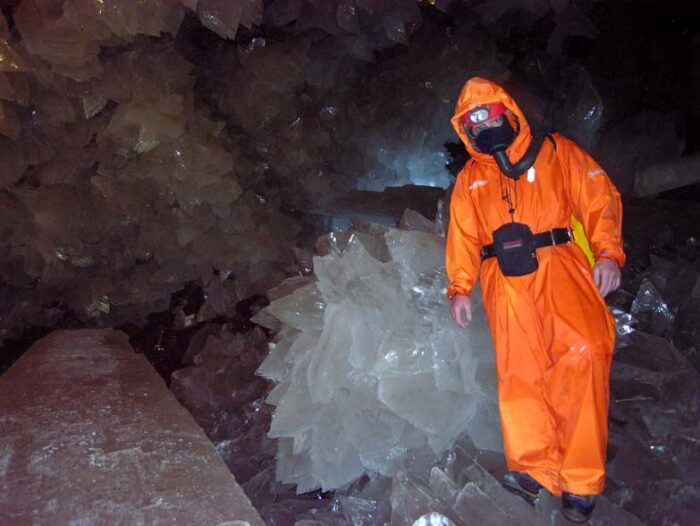 a figure in orange stands next to a crystal