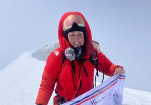 Metcalf smiles on a snowy summit, holding a banner of the clinic where she works.