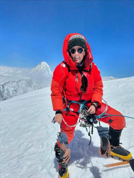 Metcalf standing on a sunny, snowy summit, the secondary point of Broad Peak behind her