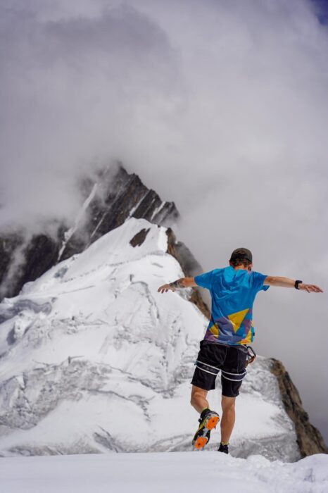 Andrews runs down a snow slope in shorts and t-shirt, with crampons attached to the sneakers