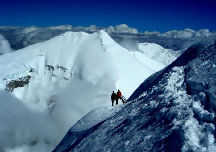 Climbers traversing a snow slope on Cho Oyu, high mountains behind them.