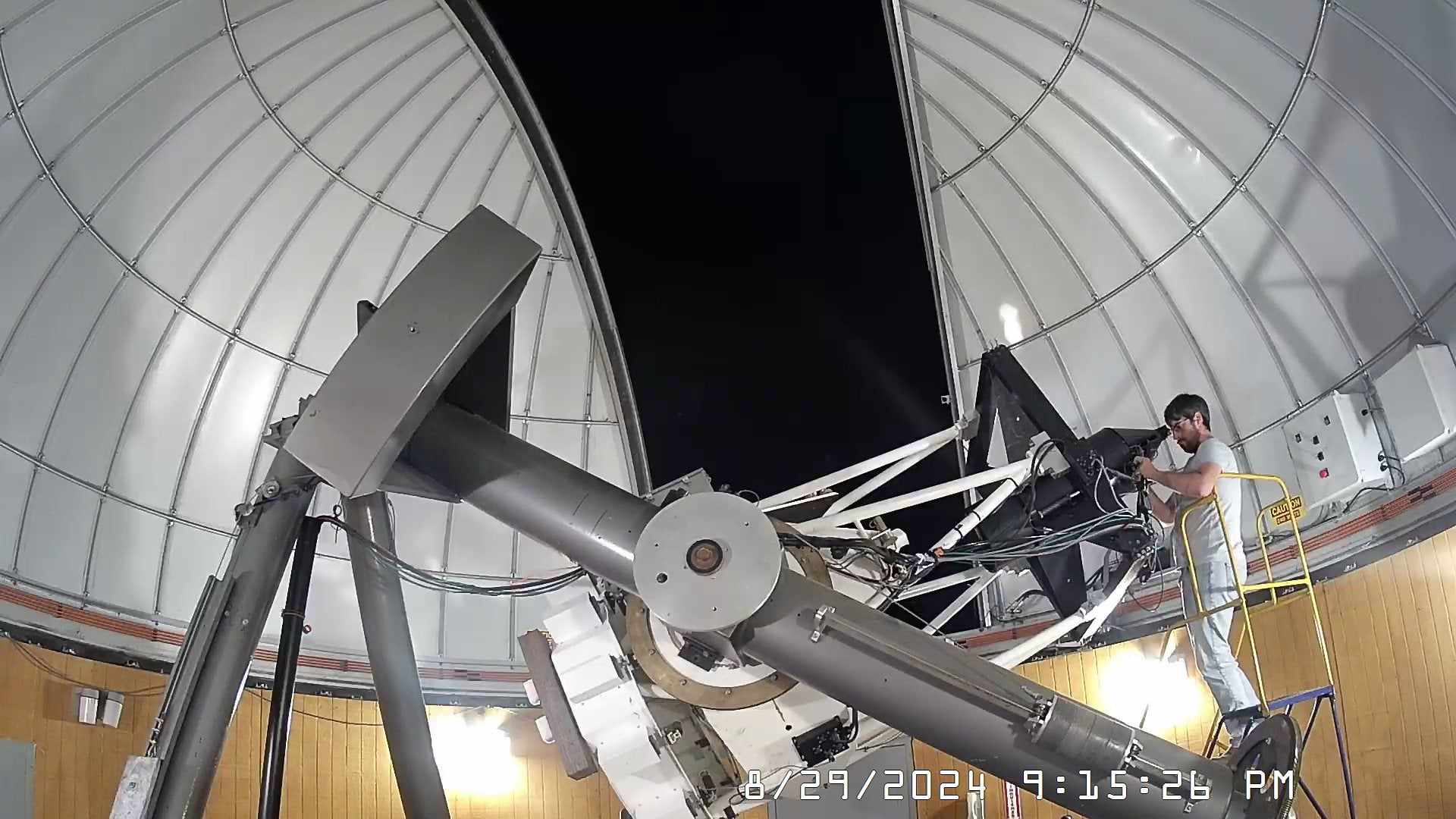 A man stands on a ladder and prepares to look through a telescope.