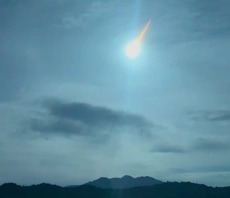 A bright light with a trail flashes in the sky above a mountain.