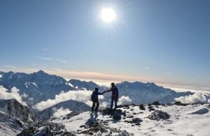 The climbers shake hands on a snowy, flat summit