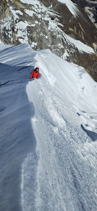 A climber on the edge of a sharp snow ridge