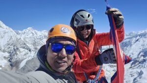 The climbers in mounaineering clothes smile on a summit