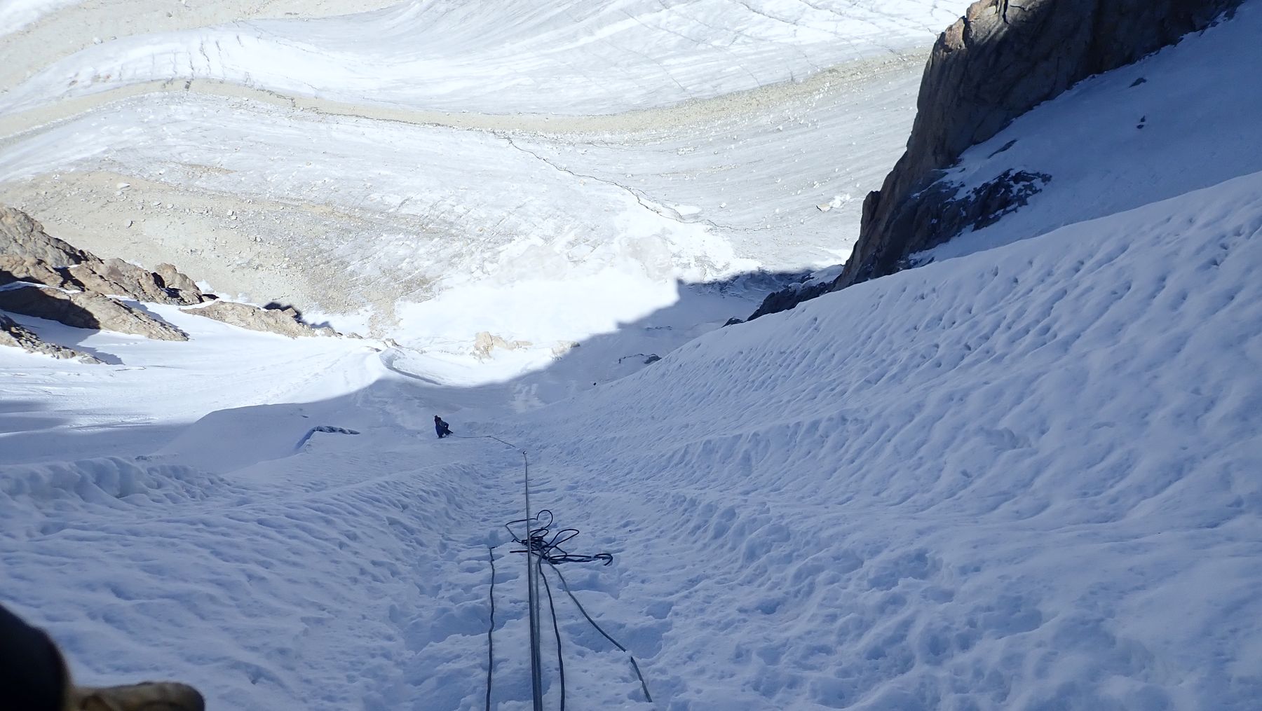 A line of tracks up a snow ramp and a climber at the bottom of it.