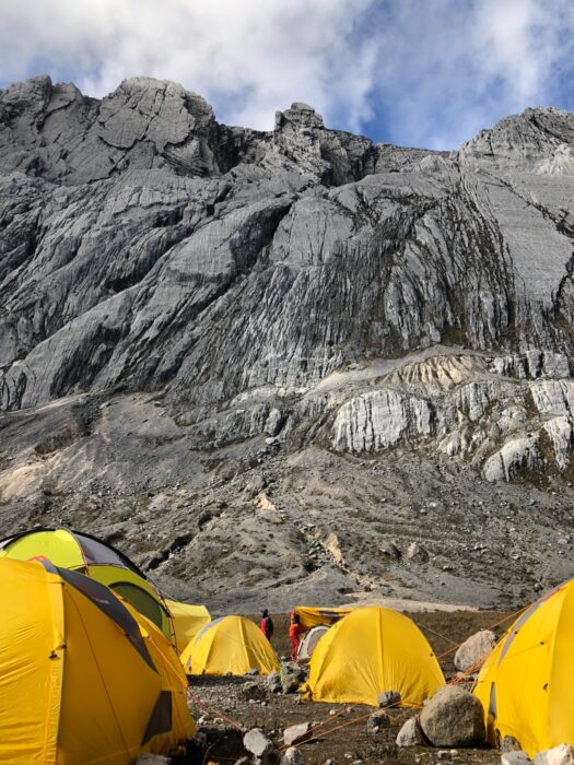 A group of yellow tents at the base of a limestone peak