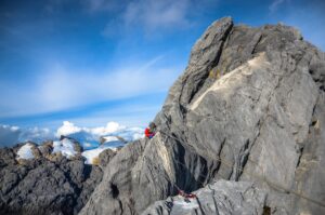 a climber on a rock spur behind a cable bridge